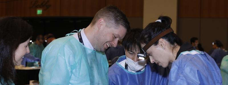 Three surgical residents practice annular enlargement on a porcine heart. 